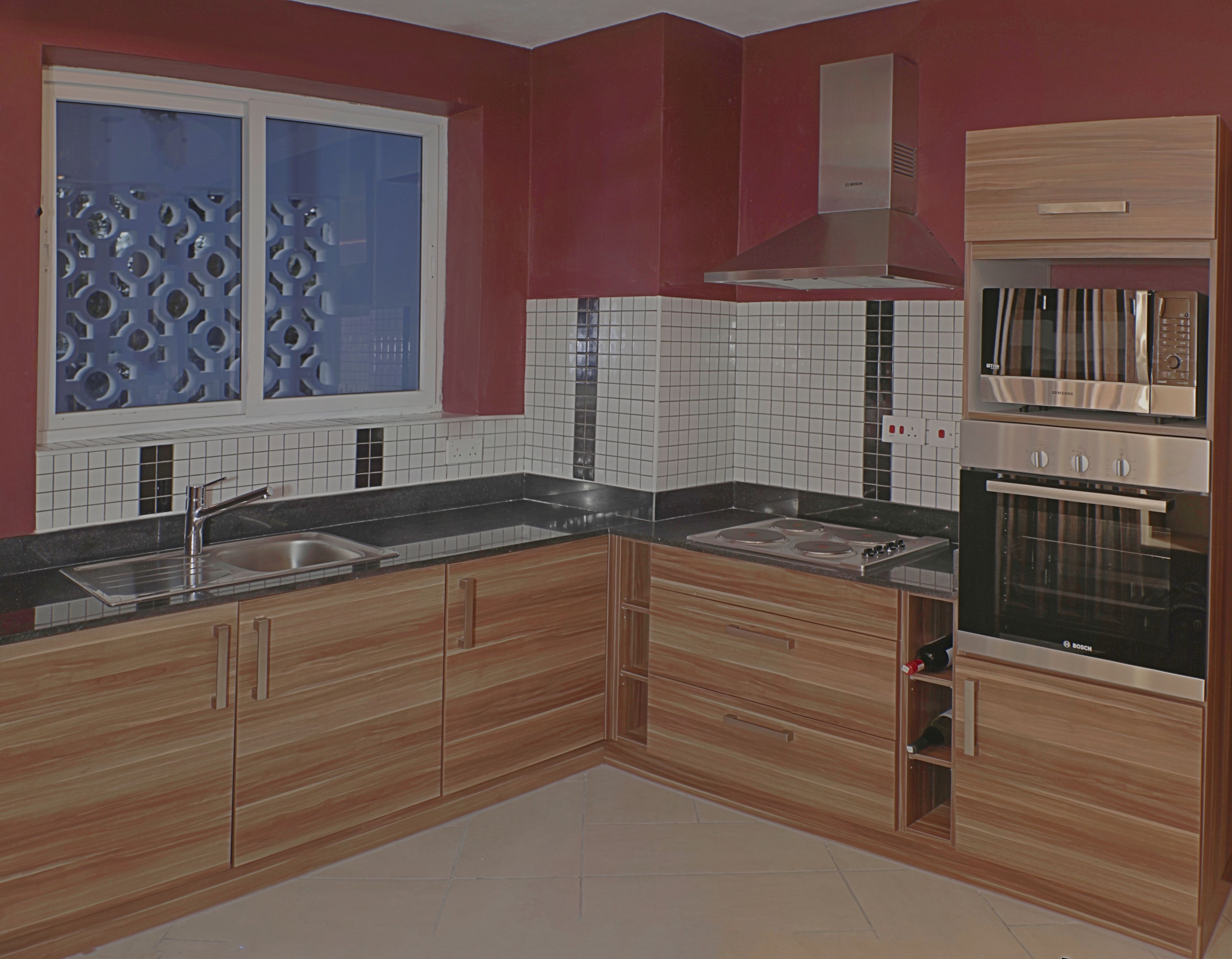 A modern kitchen with wooden cabinets, a stainless steel sink, a built-in oven, and a window with decorative glass.