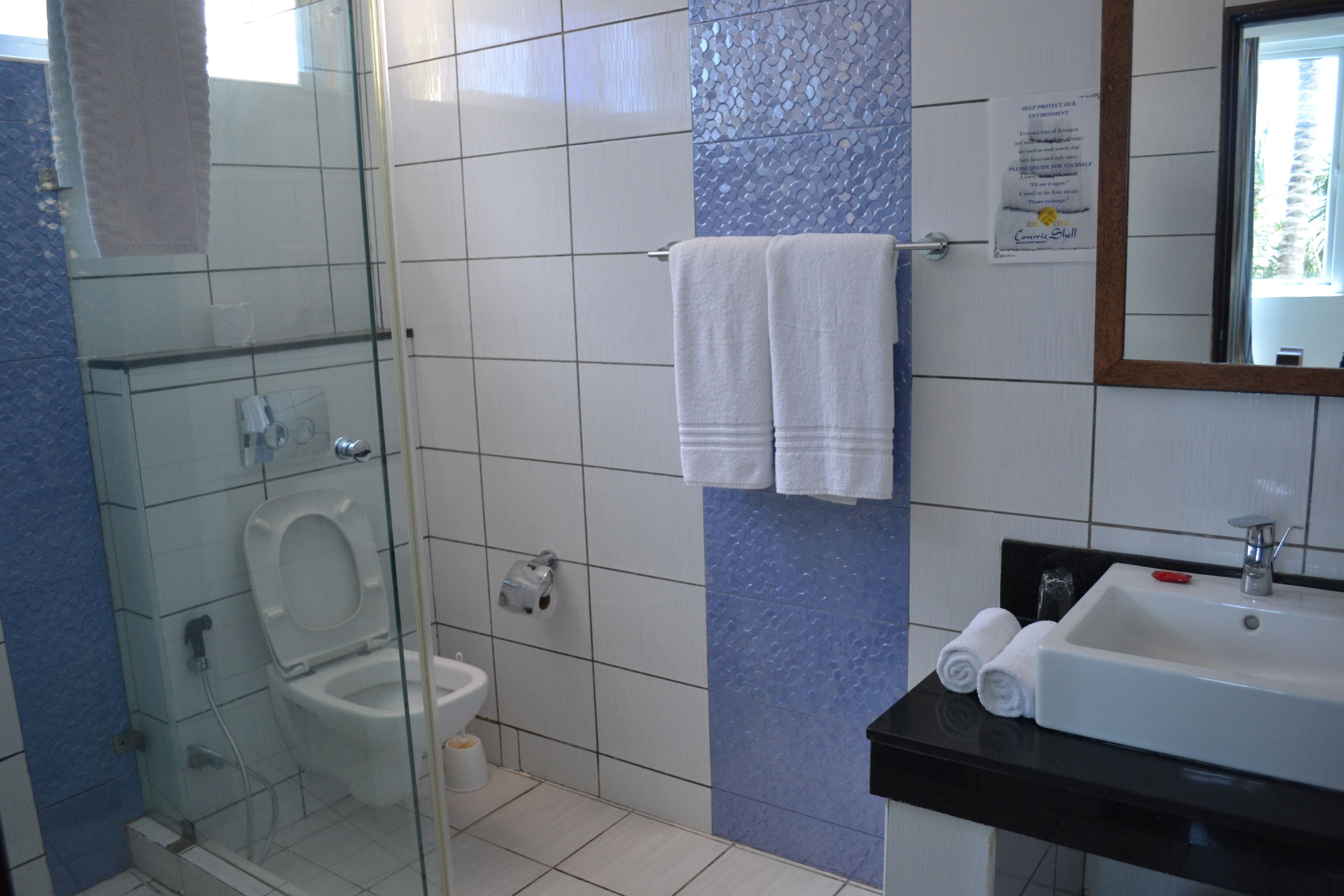 A bathroom with a glass-enclosed shower, a white toilet, a sink with a black countertop, and two towels hanging on the wall.