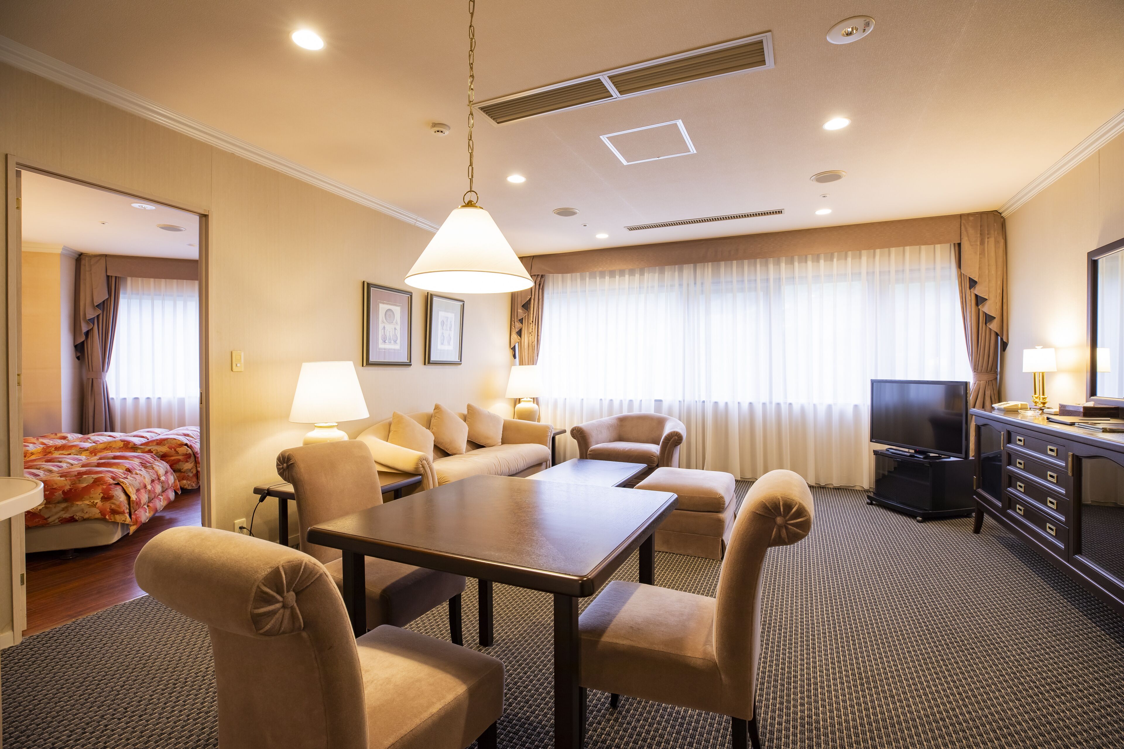 A hotel room with a dining area, a sofa set, a TV, and a desk with drawers.