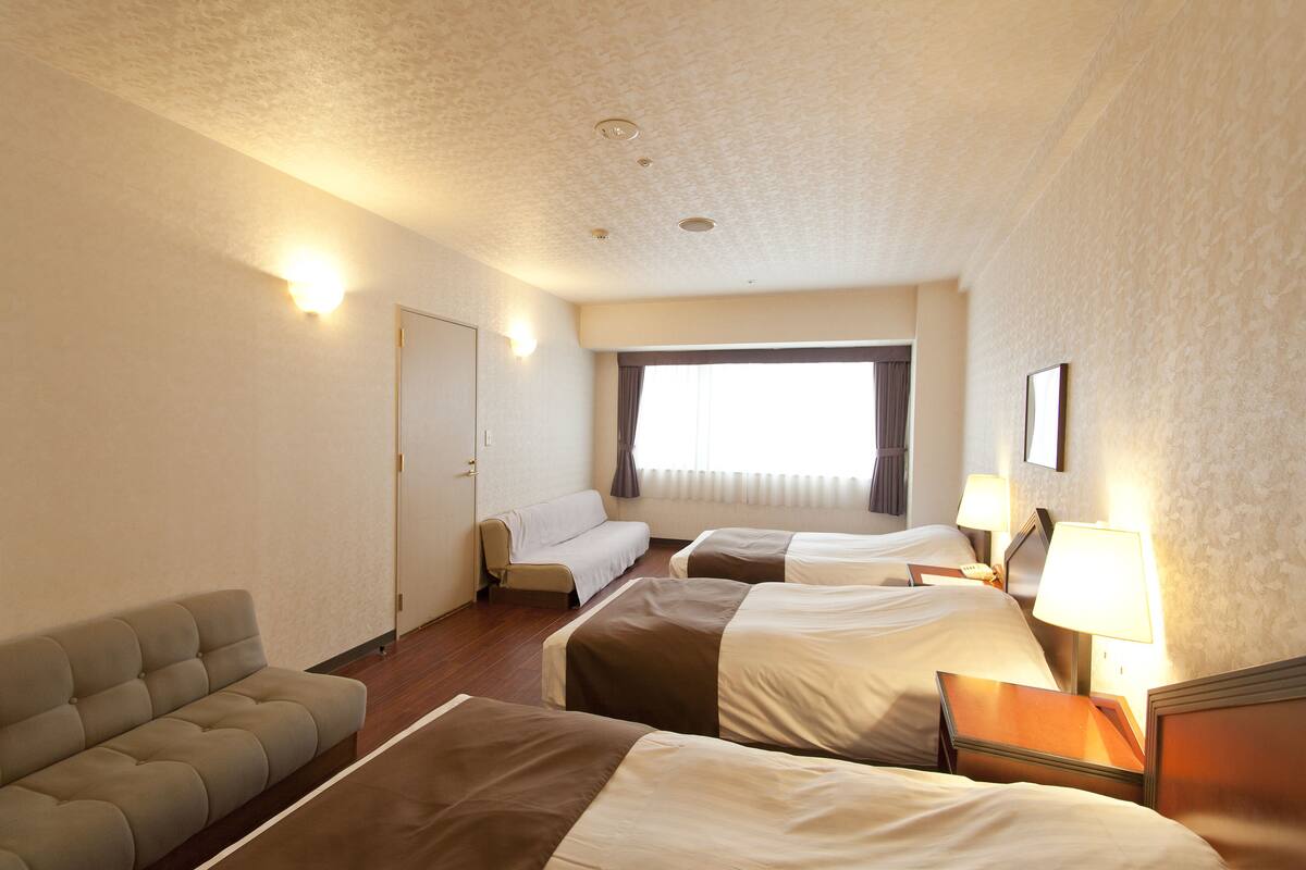 A hotel room with two beds, a sofa, and a window with curtains.