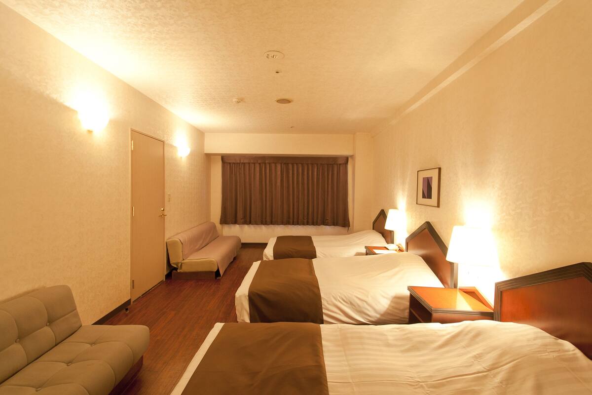 A hotel room with two beds, a sofa, a desk, and a window with curtains.