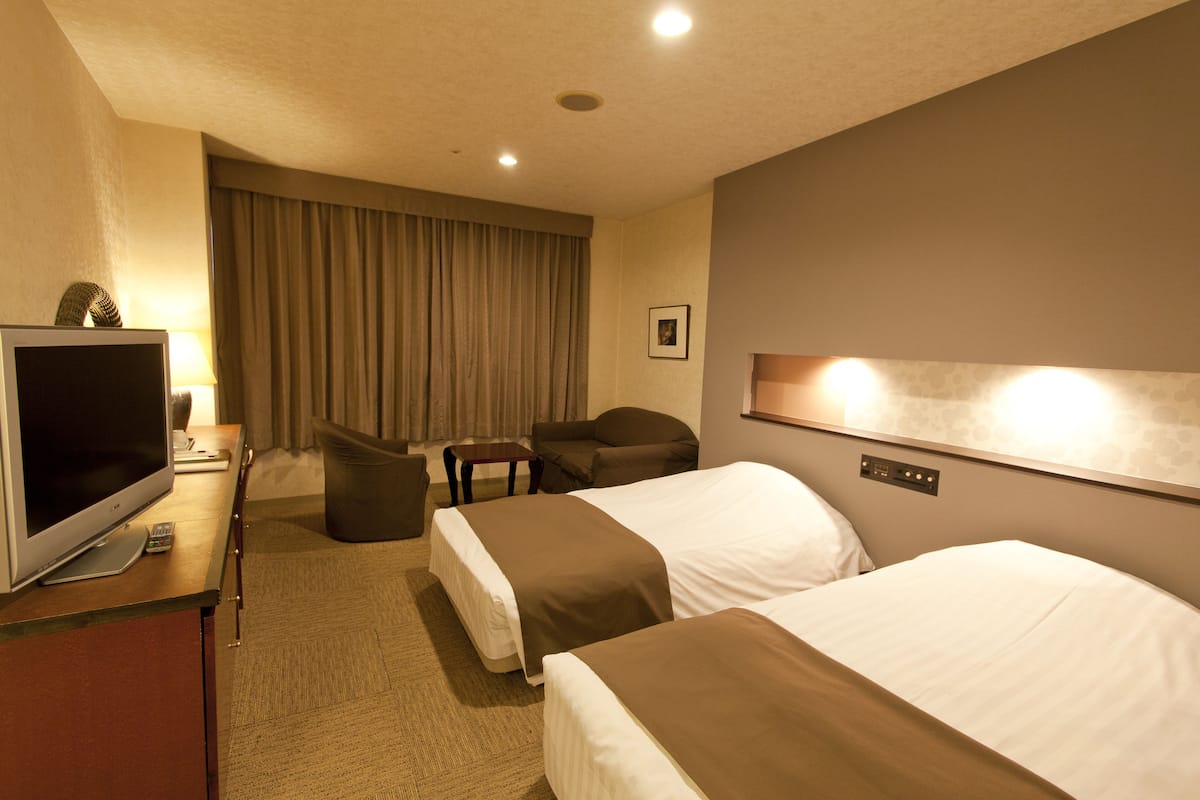 A hotel room with two beds, a TV, a desk, and a chair.