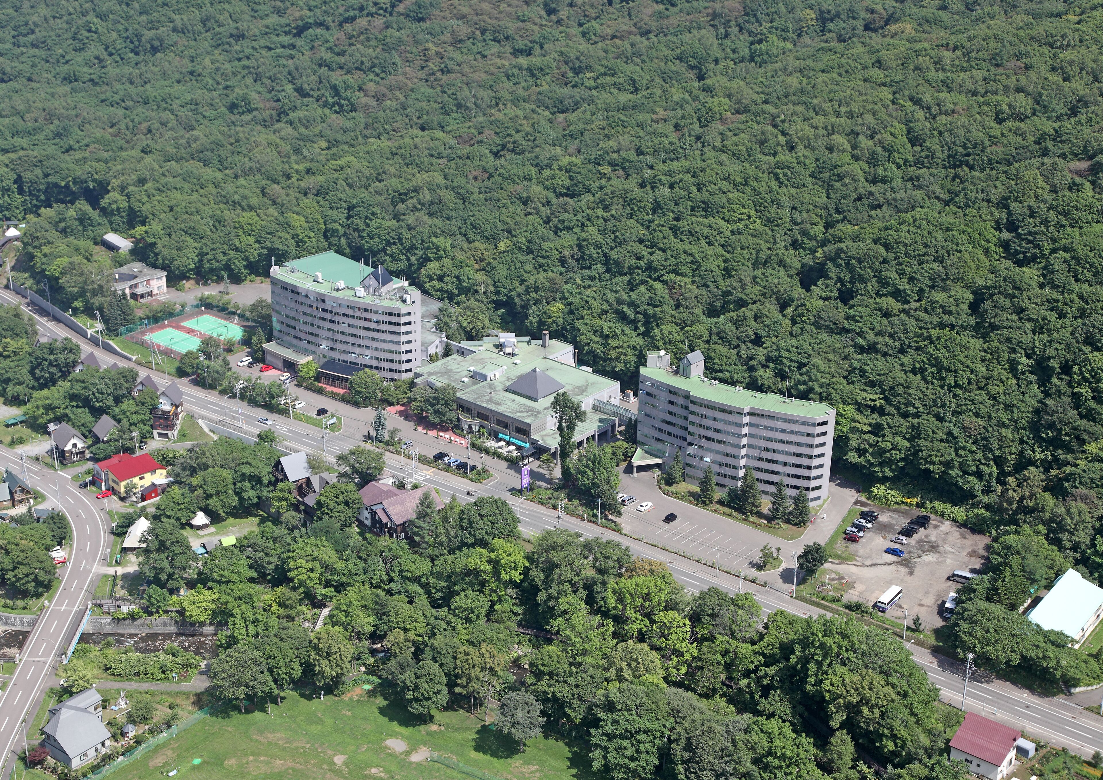 An aerial view of a hotel complex with multiple buildings, surrounded by dense forest.