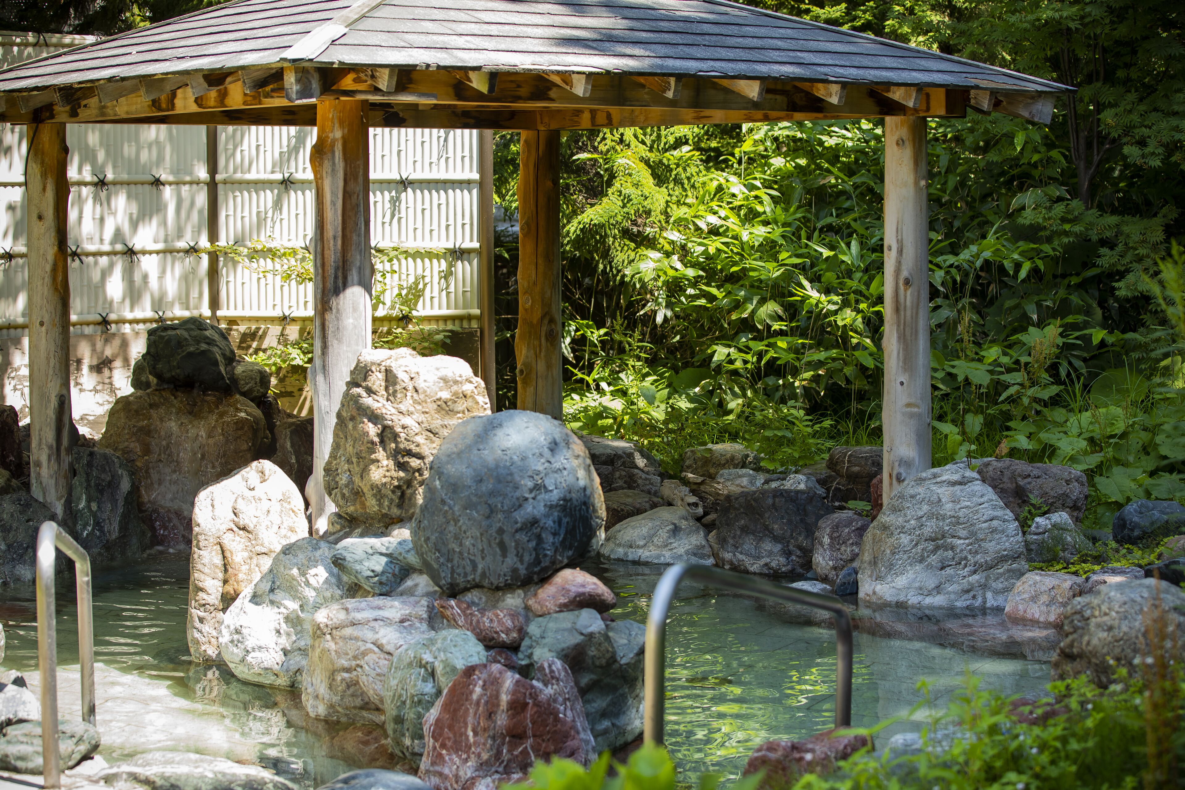 Ein hölzerner Pavillon mit einem Ziegeldach, umgeben von Steinen und einem kleinen Teich.