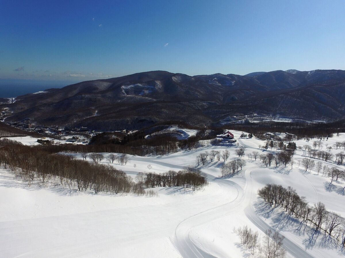 A snow-covered landscape with a winding road, mountains in the background, and a clear sky.