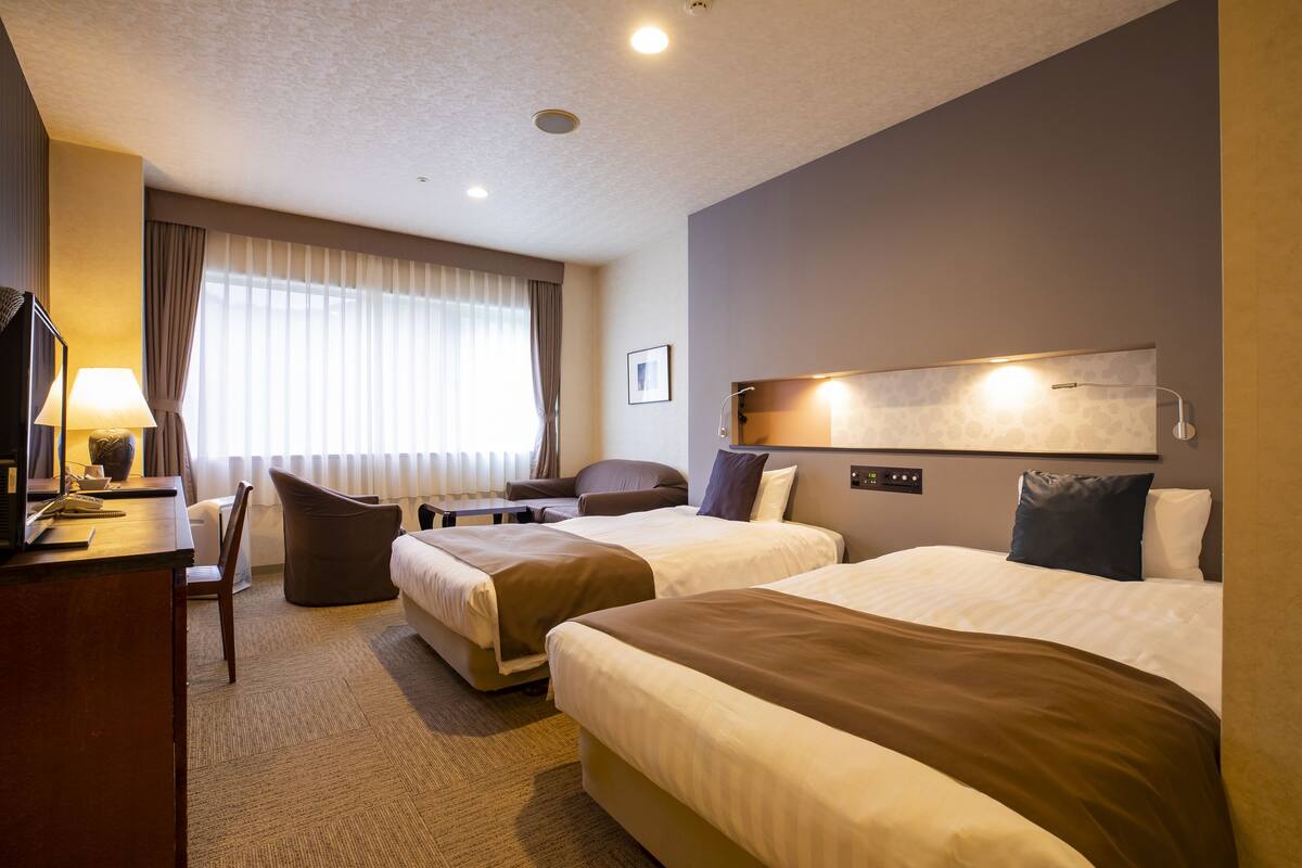 A hotel room with two beds, a desk, a chair, and a TV.