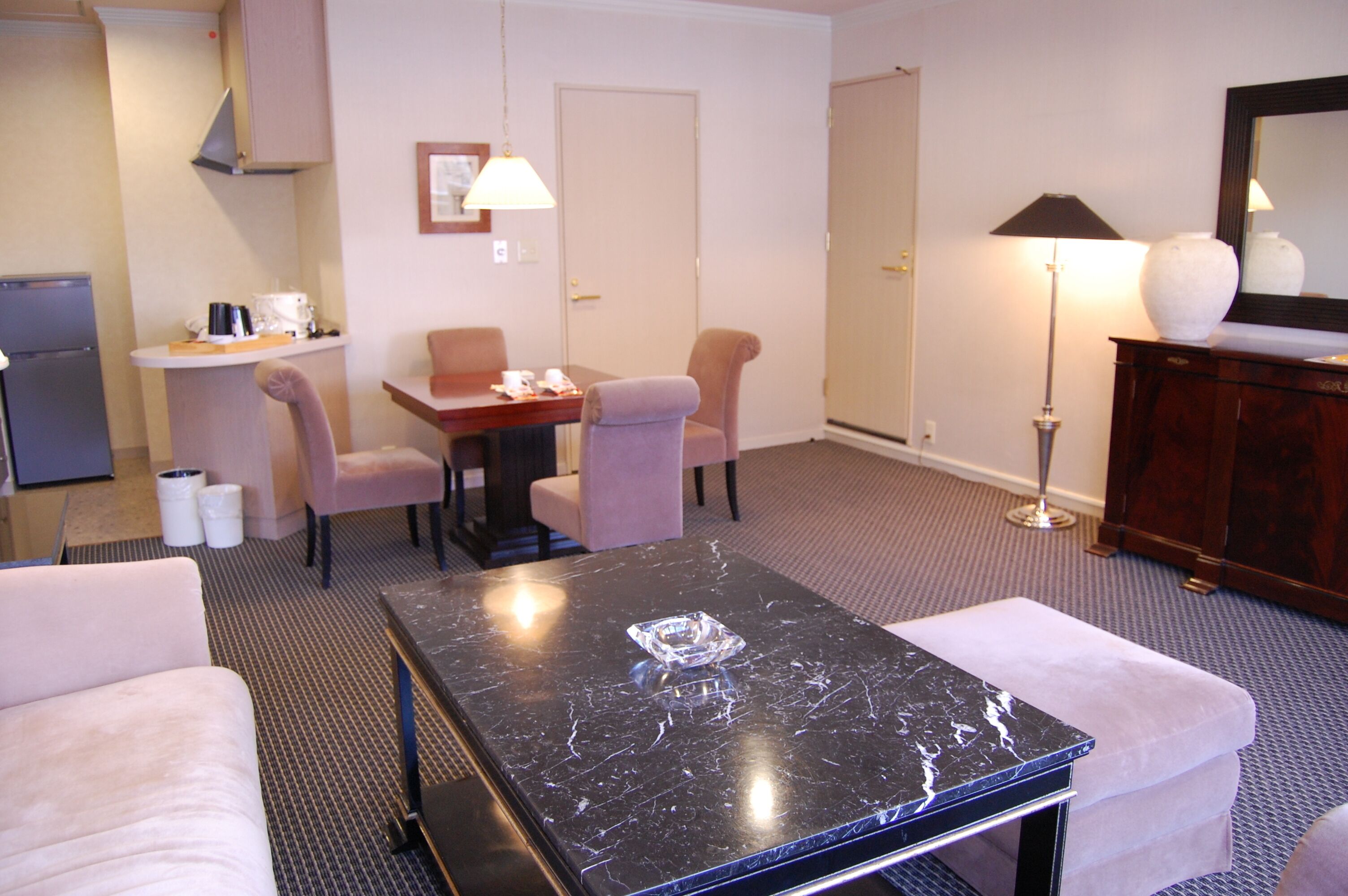 Une chambre d’hôtel comprenant un coin repas, un canapé, une table agrémentée d’un objet décoratif, une lampe et un meuble.