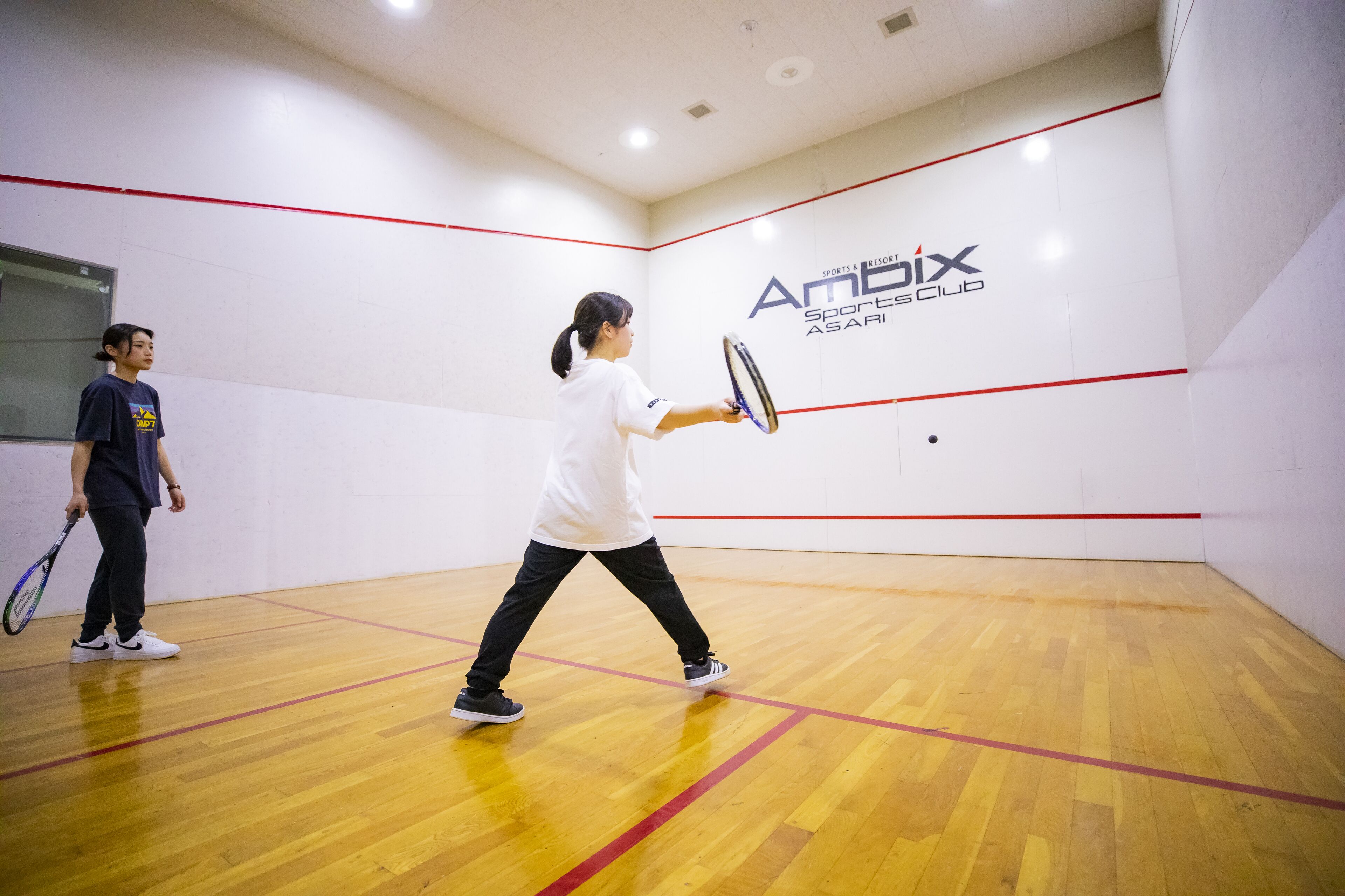 A squash court with a wooden floor and red boundary lines.