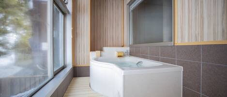 A modern bathroom with a freestanding bathtub, a window, and wooden flooring.
