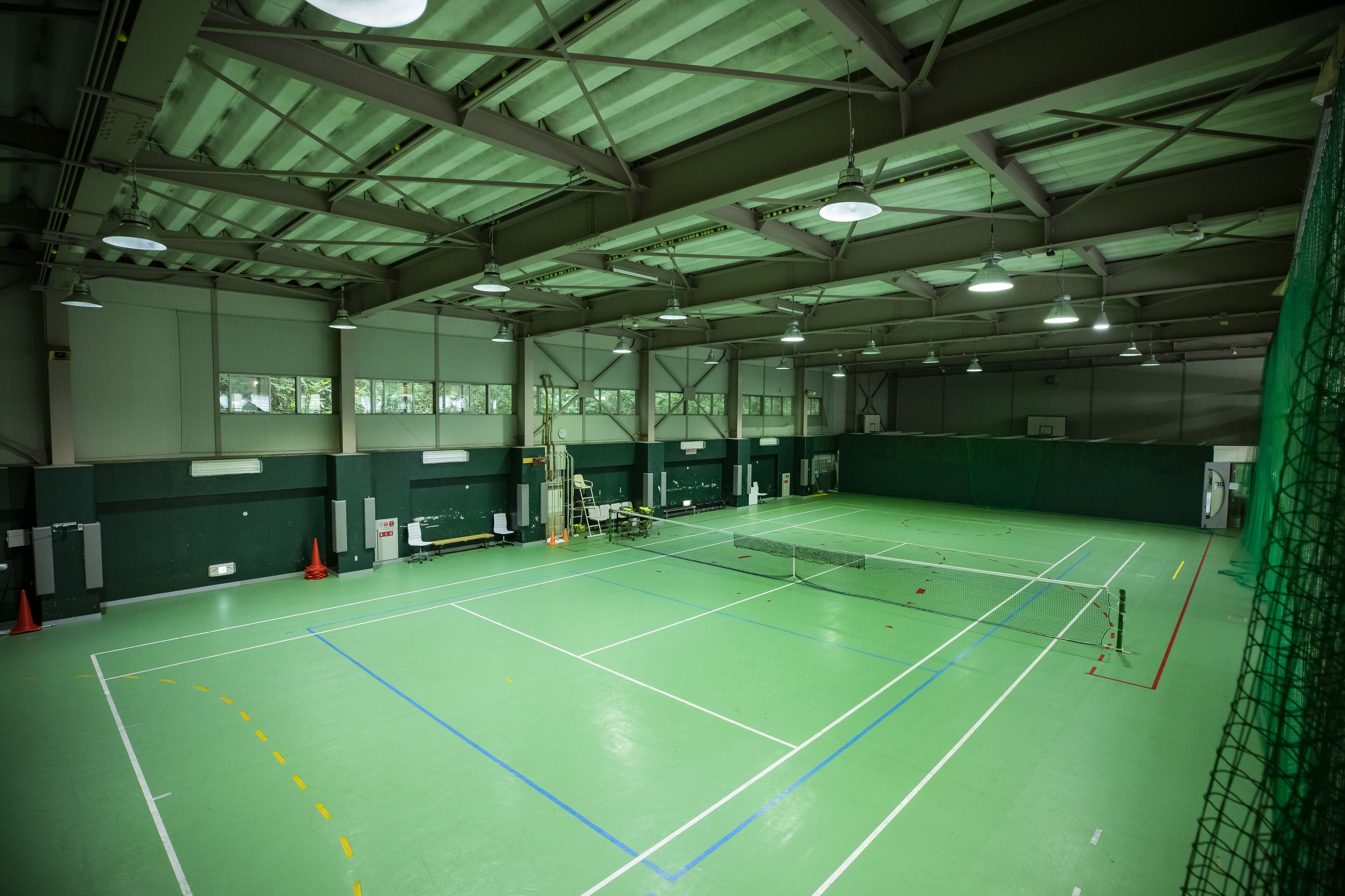 Una cancha de bádminton interior con piso verde, líneas blancas delimitadoras y una red.