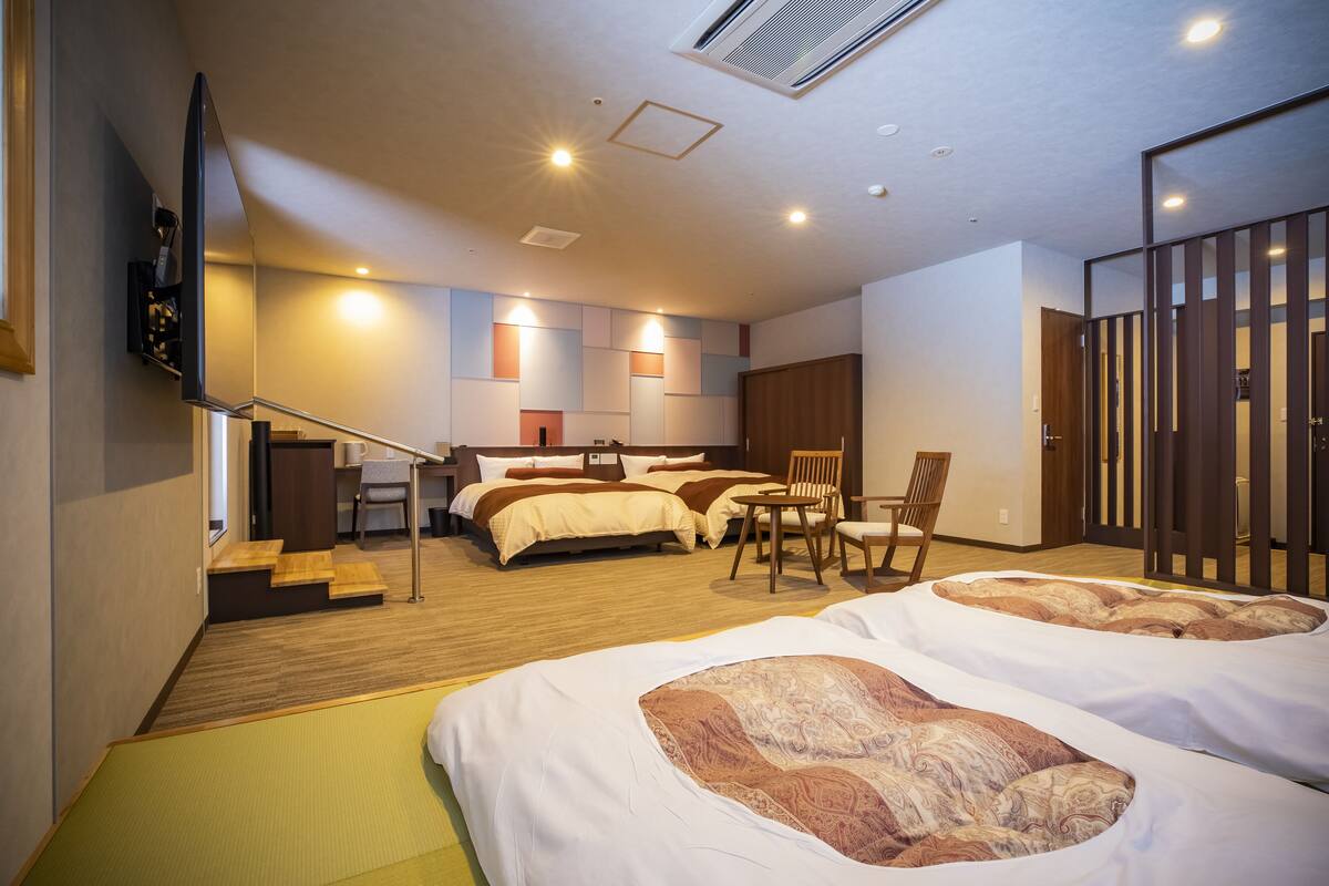 A hotel room with two beds, a sitting area, and a staircase leading to an upper level.