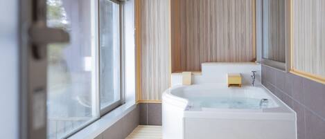 Un baño moderno con una bañera grande, una ventana y piso de madera.