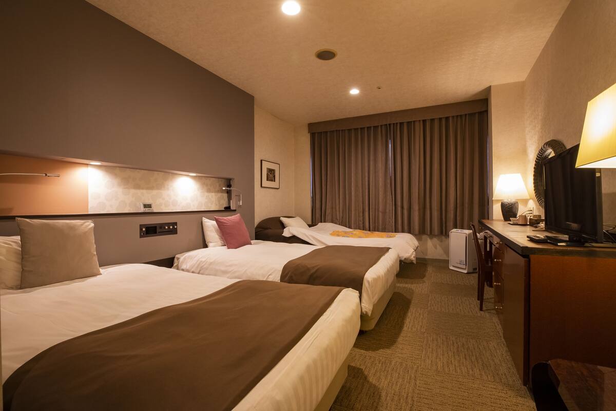 A hotel room with two beds, a desk, a chair, a television, and a window with curtains.