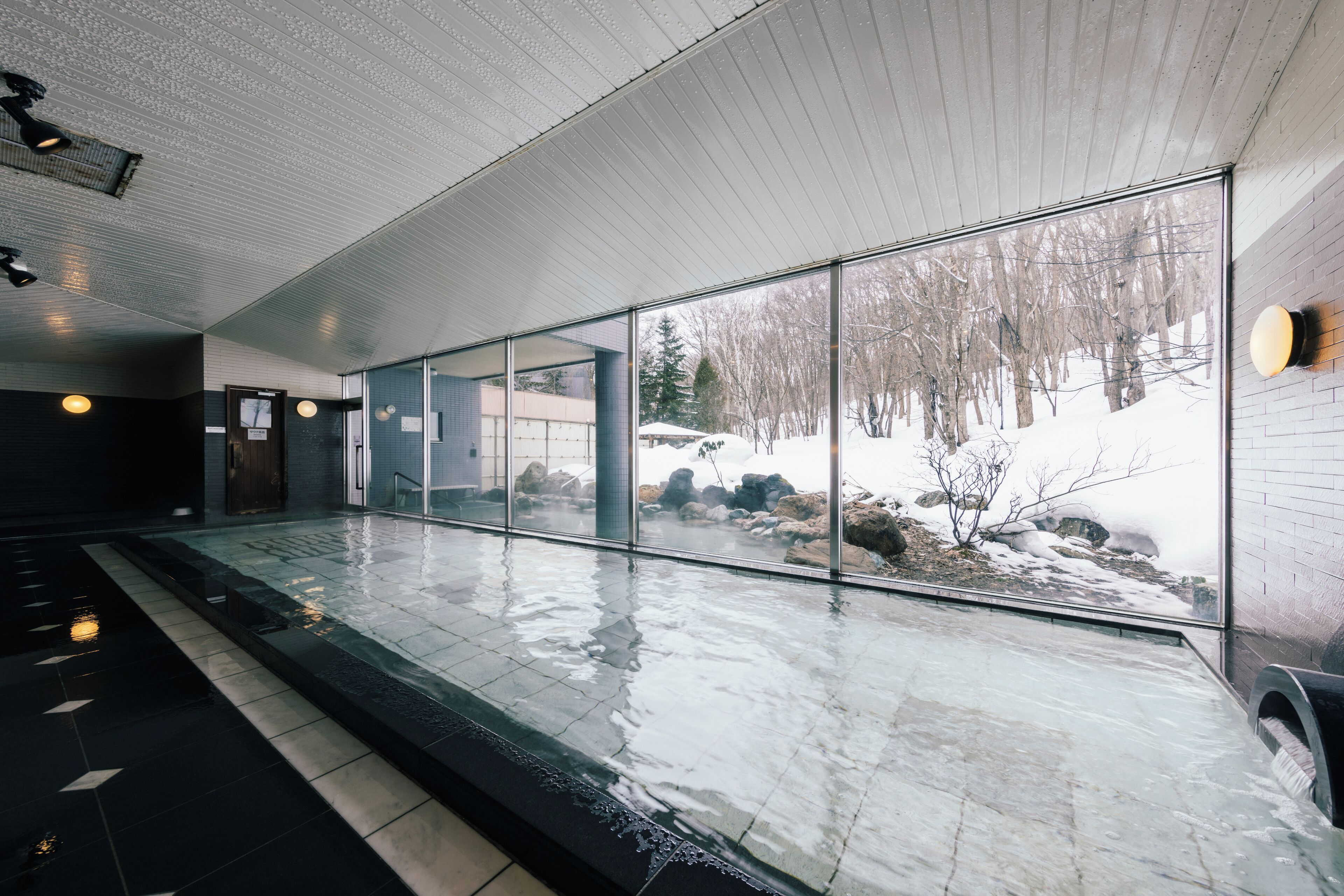 Ein moderner Poolbereich im Innenbereich mit Glaswänden, gefliestem Boden und Blick auf eine verschneite Winterlandschaft.