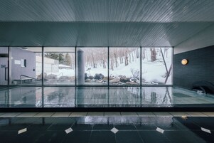 A modern indoor pool with large windows offering a view of a snowy outdoor landscape.