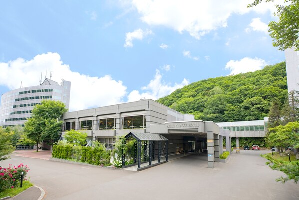 A modern hotel with a covered entrance, lush greenery, and a parking area. - Asari Classe Hotel (Otaru)