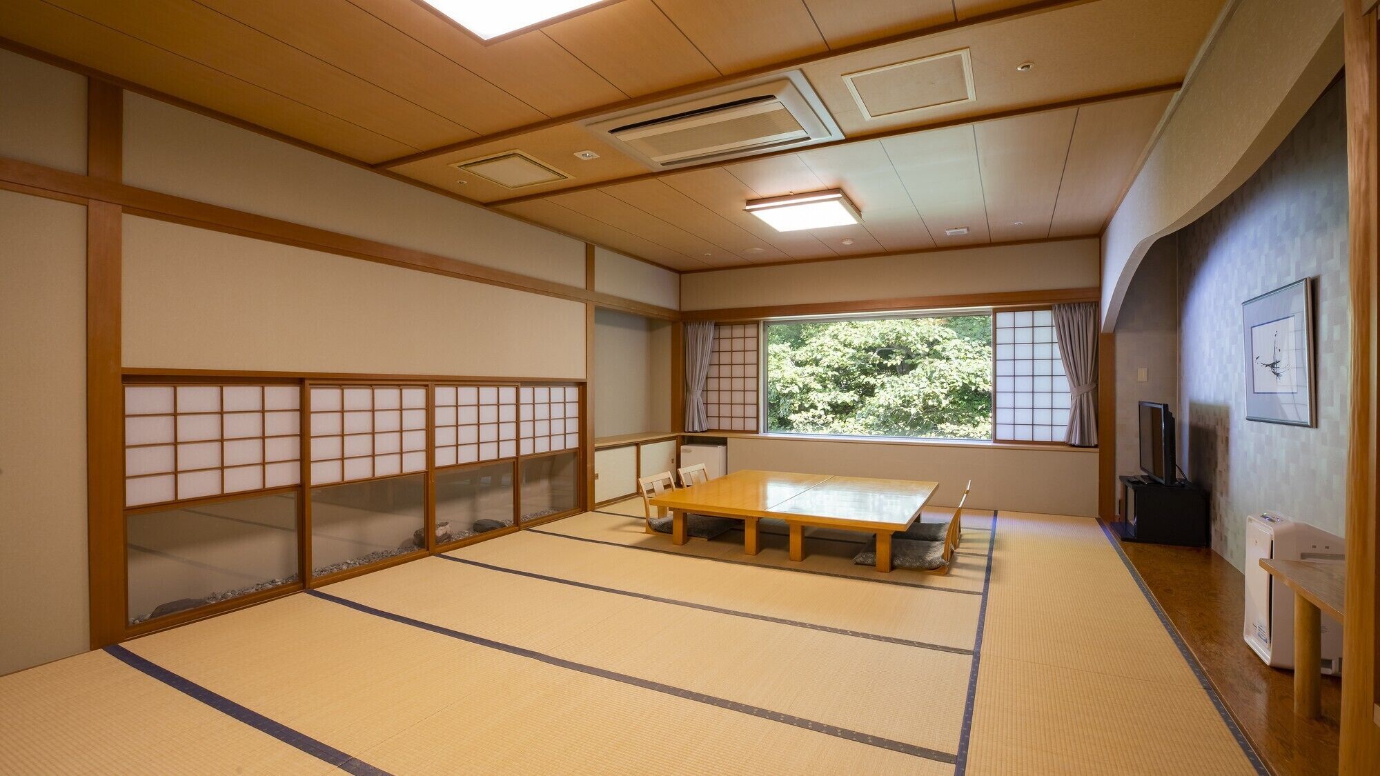 A tatami mat room with a wooden table, sliding doors, and a view of trees.