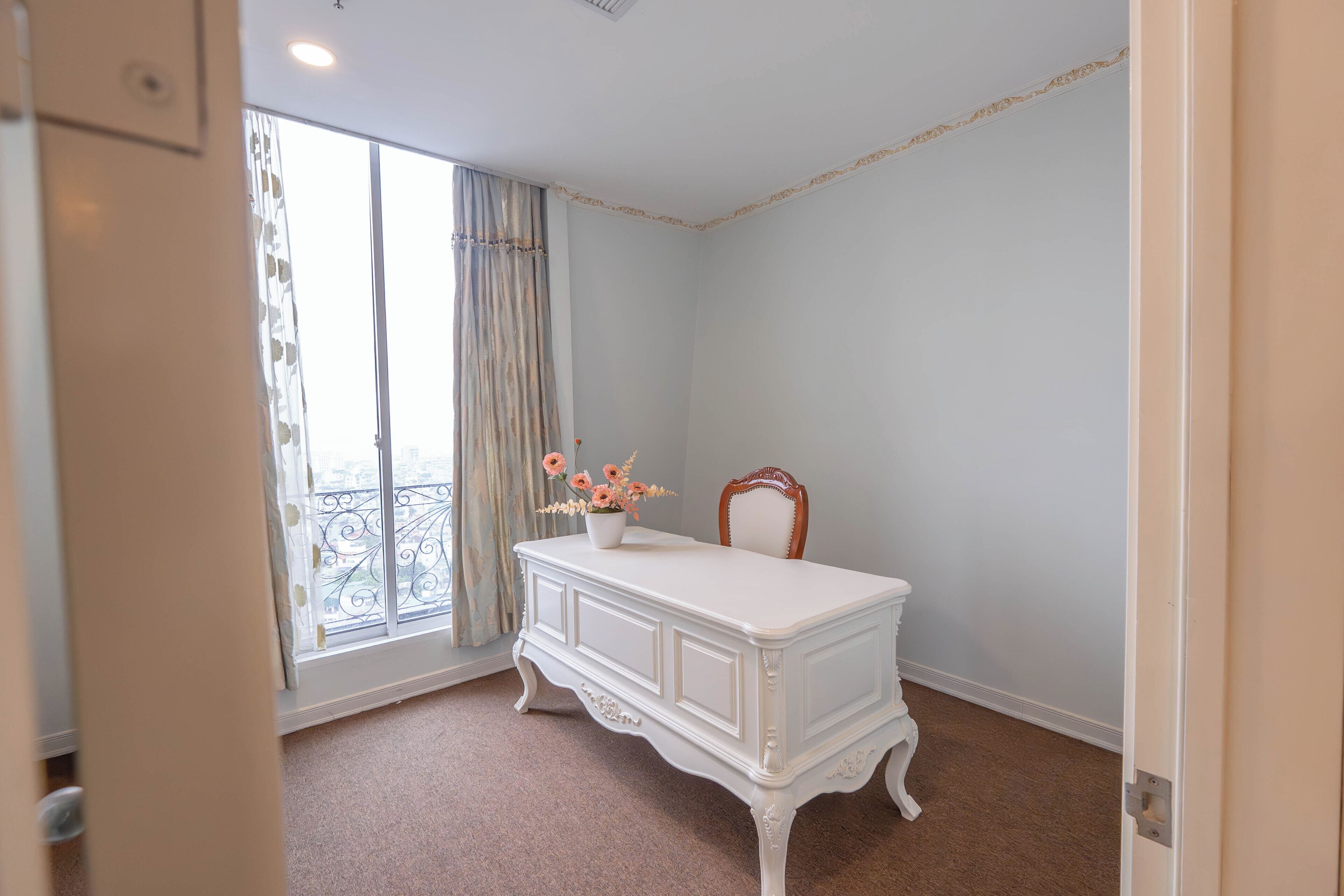 A room with a white dresser, a chair, a window with curtains, and a balcony.