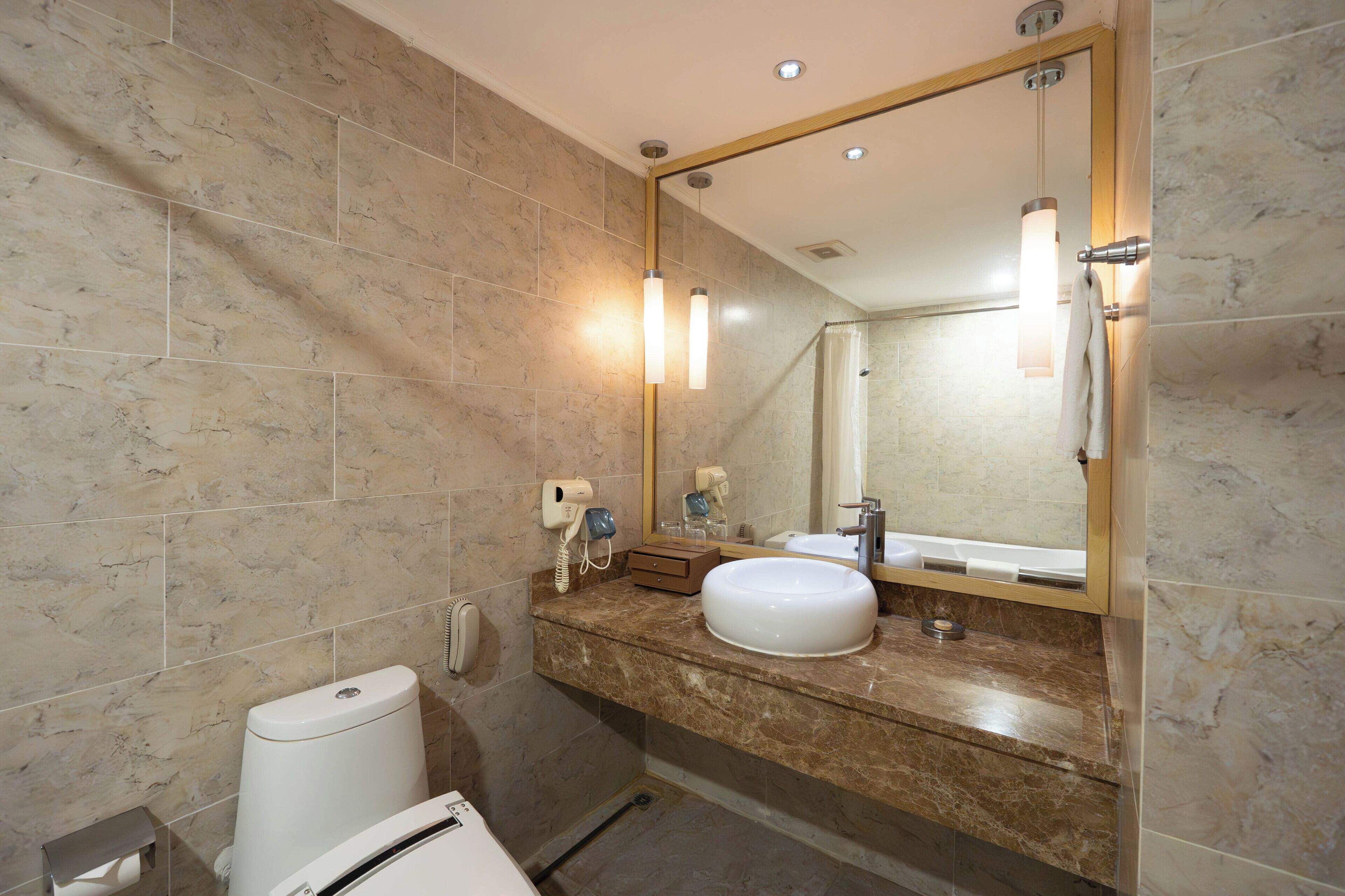 Un baño con pared de azulejos de mármol, un lavamanos, un espejo, un perchero para toallas y un cabezal de ducha de mano.