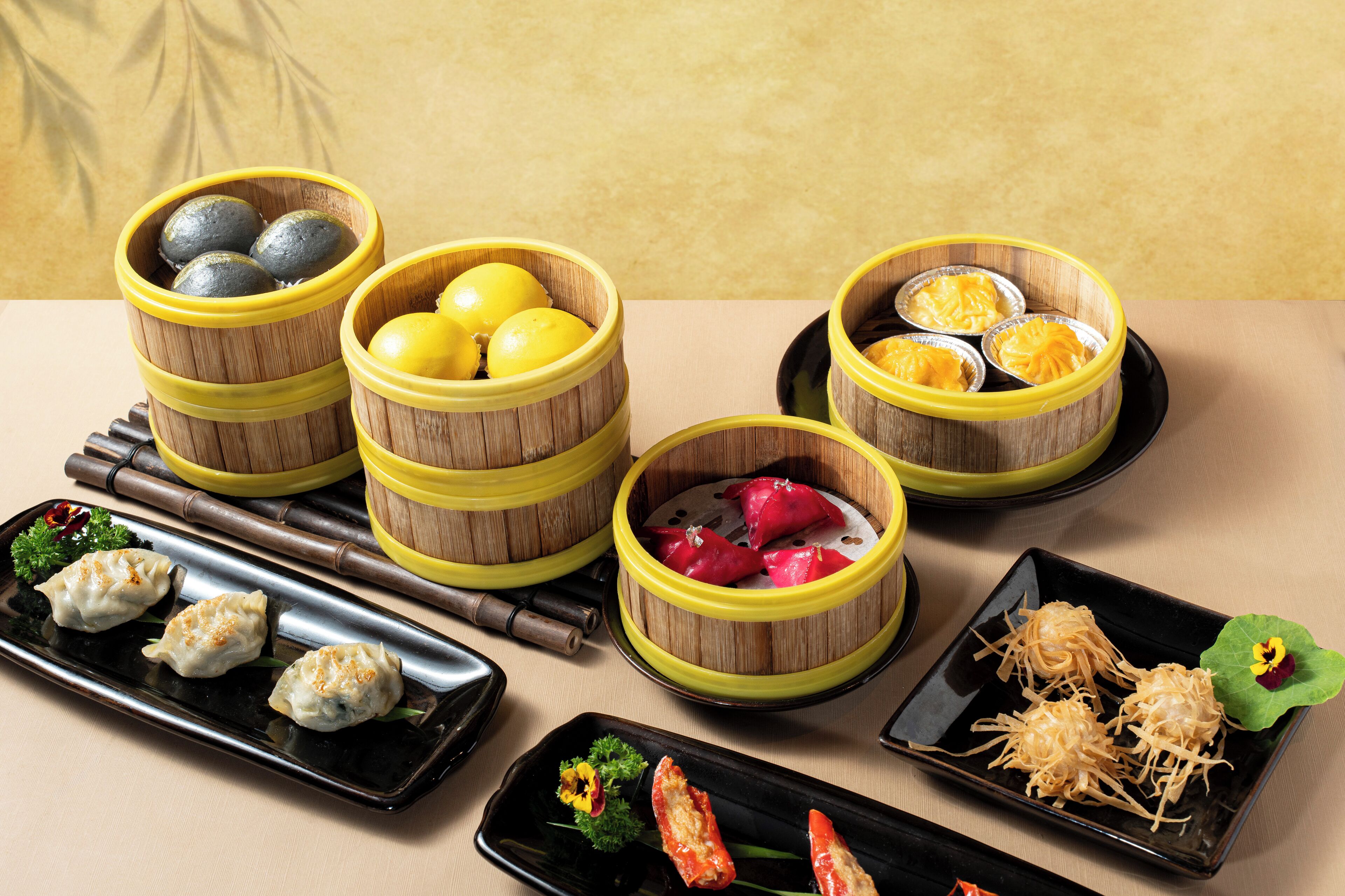 A variety of Asian dishes, including dumplings and seafood, served on black plates and in bamboo steamers.