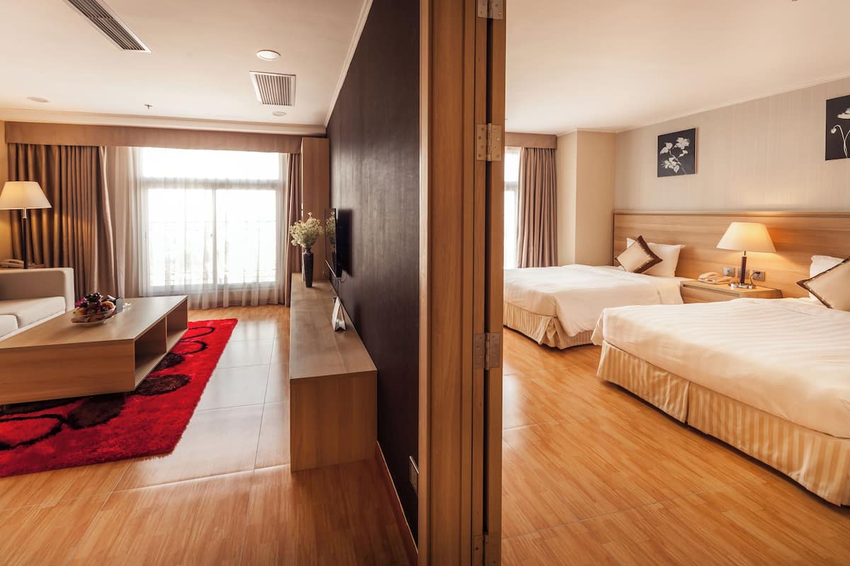 Hotellihuone, jossa on sohva, kaksi sänkyä, televisio, työpöytä ja punainen matto.
