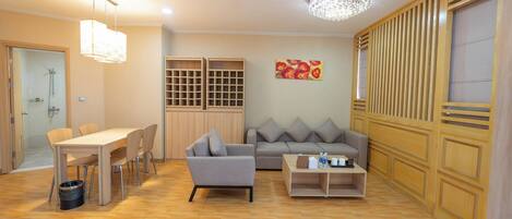 A modern living room with a dining table, sofa, and coffee table. There is a wooden partition with slats, a chandelier, and a painting on the wall.