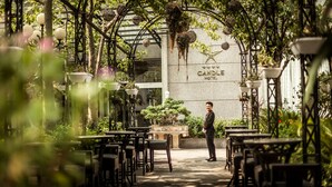 An outdoor seating area with tables and chairs, a man standing, and a building with 'CANDLE HOTEL' written on it. - Super Candle Hotel (Hanoi)