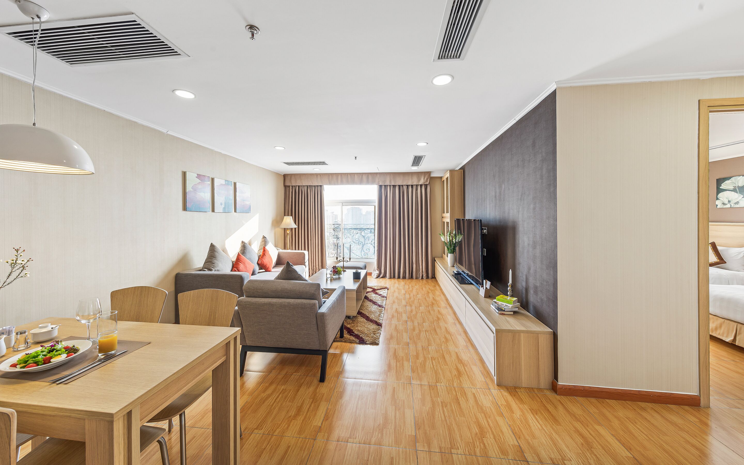 Habitación de hotel moderna con comedor, sofá, televisor y vista a la ciudad.