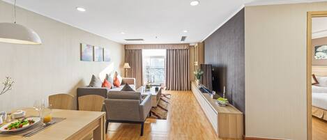 Habitación de hotel moderna con comedor, sofá, televisor y vista a la ciudad.