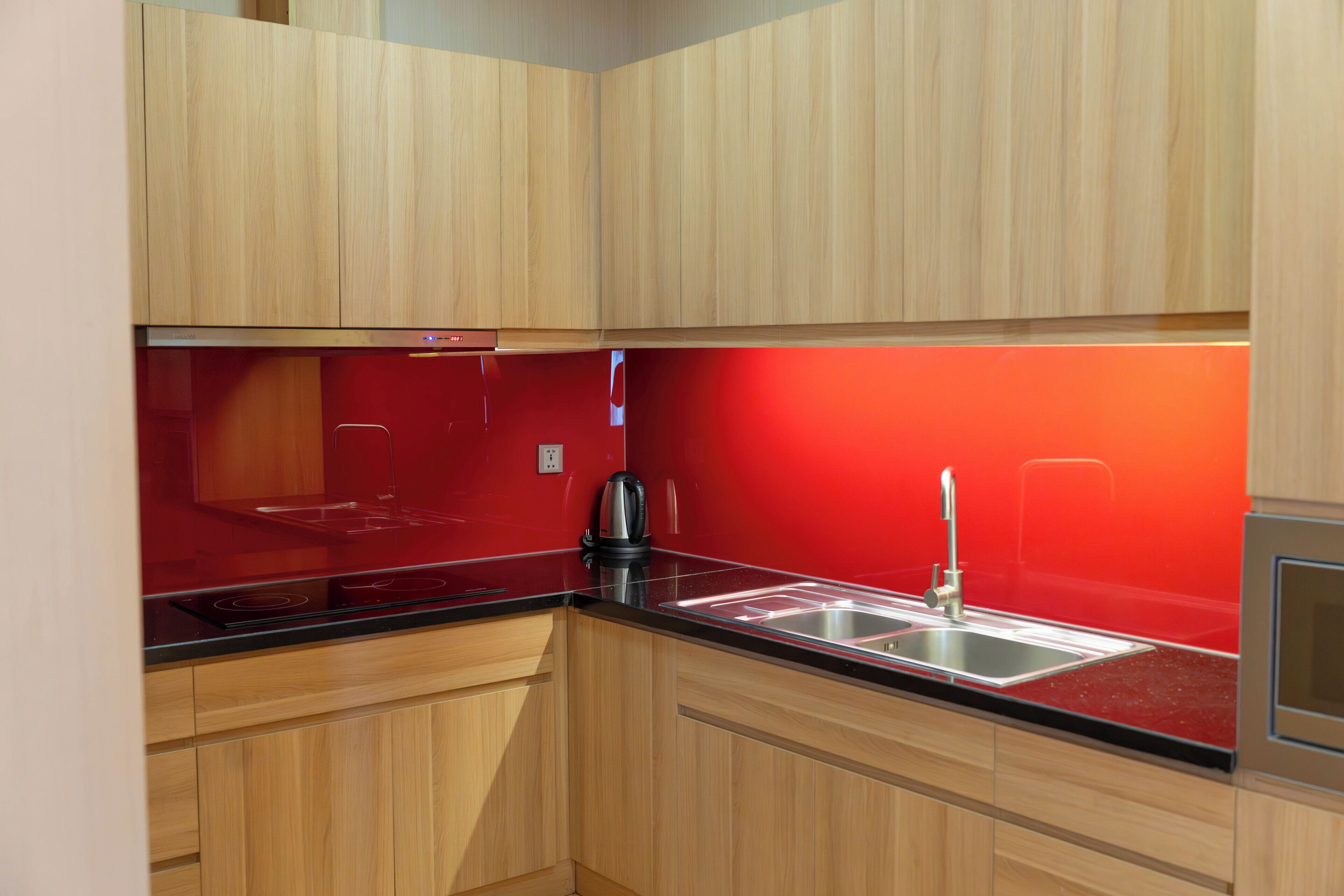A compact kitchen with wooden cabinets, a black countertop, and a red backsplash.