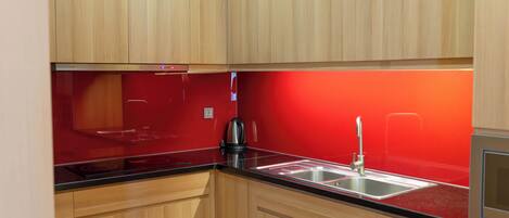 A compact kitchen with wooden cabinets, a black countertop, and a red backsplash.