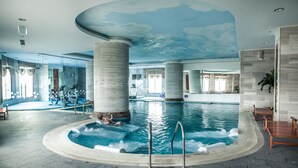 A large indoor swimming pool with a ceiling mural, concrete pillars, and a seating area with a view of the pool. - Super Candle Hotel (Hanoi)