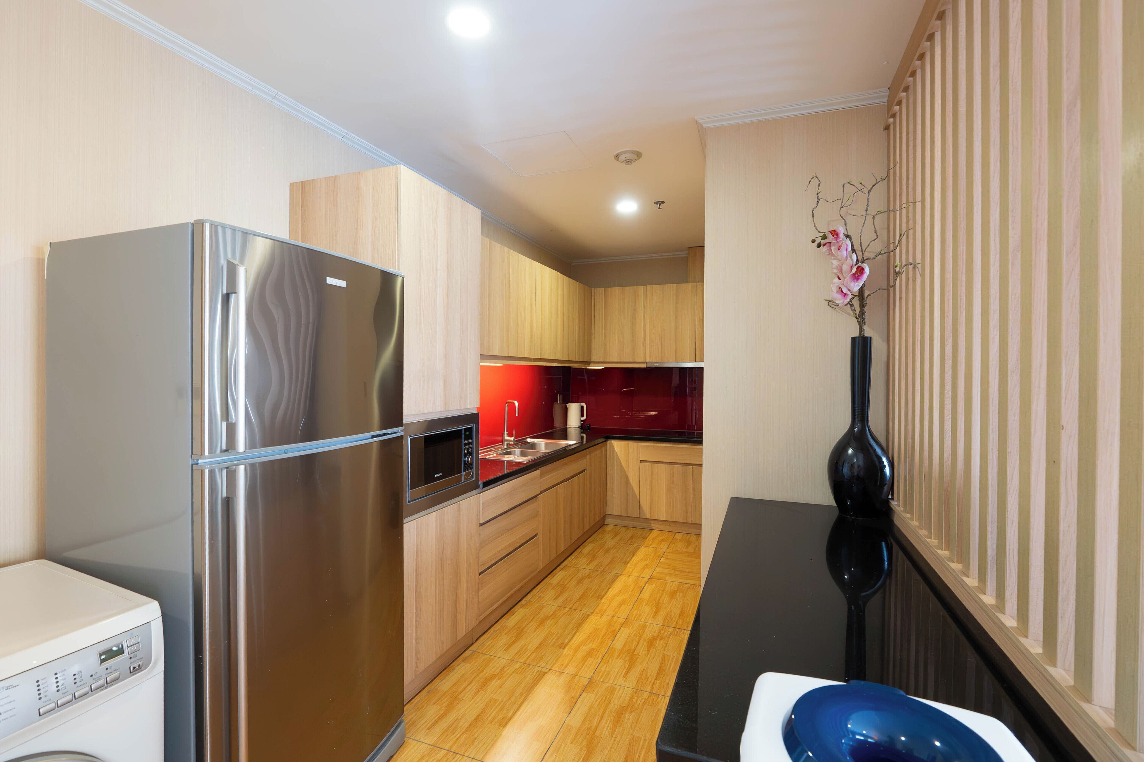 A modern kitchen with a stainless steel refrigerator, wooden cabinets, and a black vase with flowers.