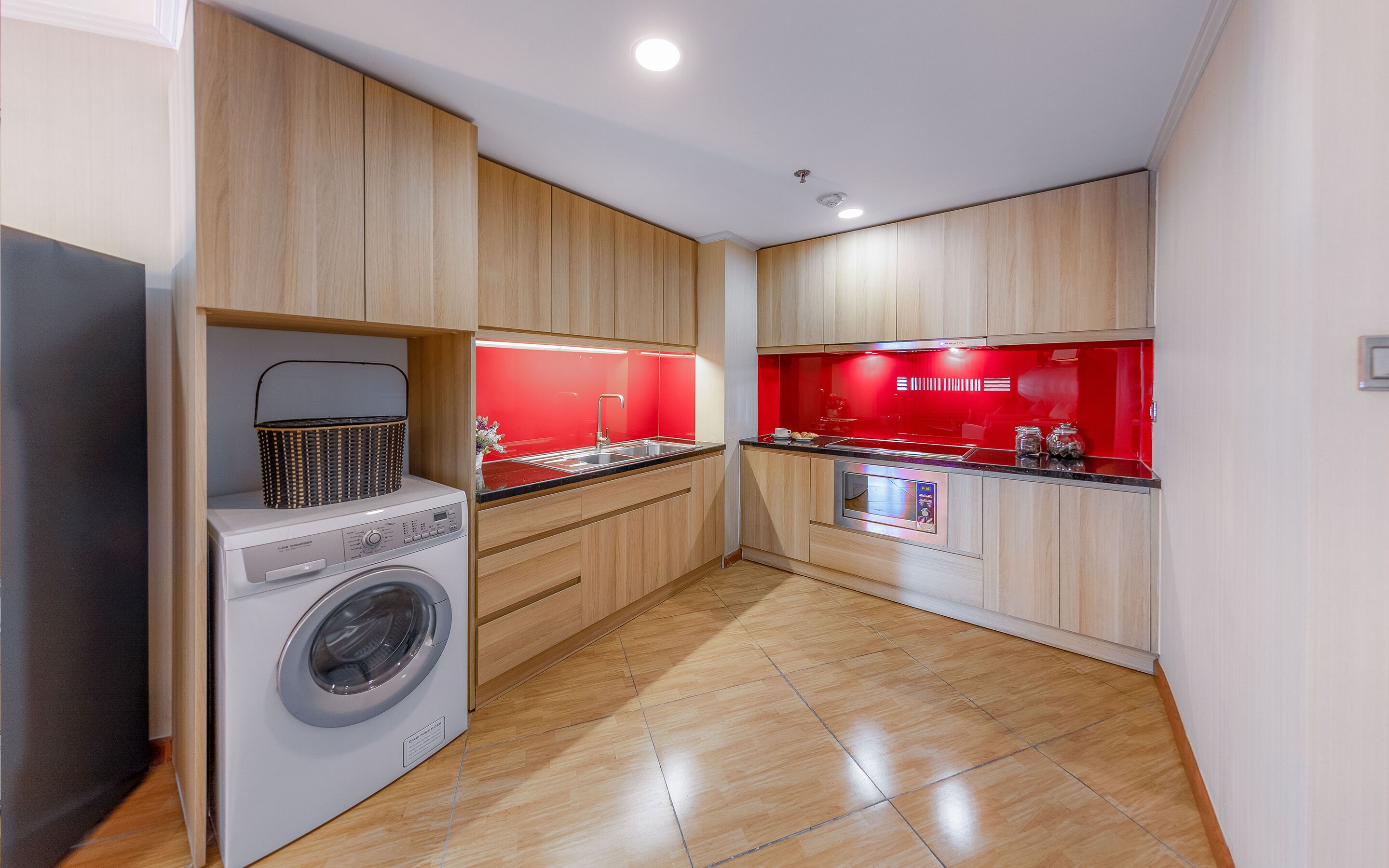 Cocina compacta con muebles de madera, lavadora y salpicadero rojo.