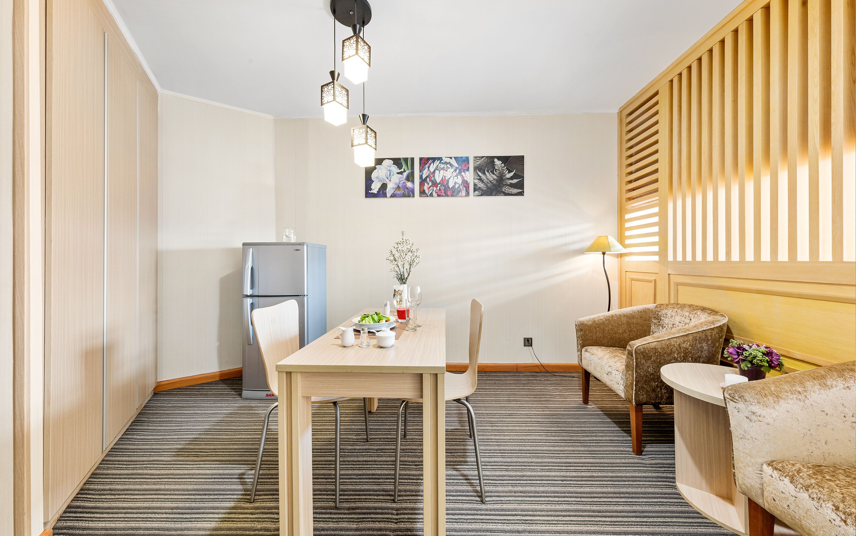 A compact living space with a dining area, a sofa, a small refrigerator, and a wall-mounted lamp.