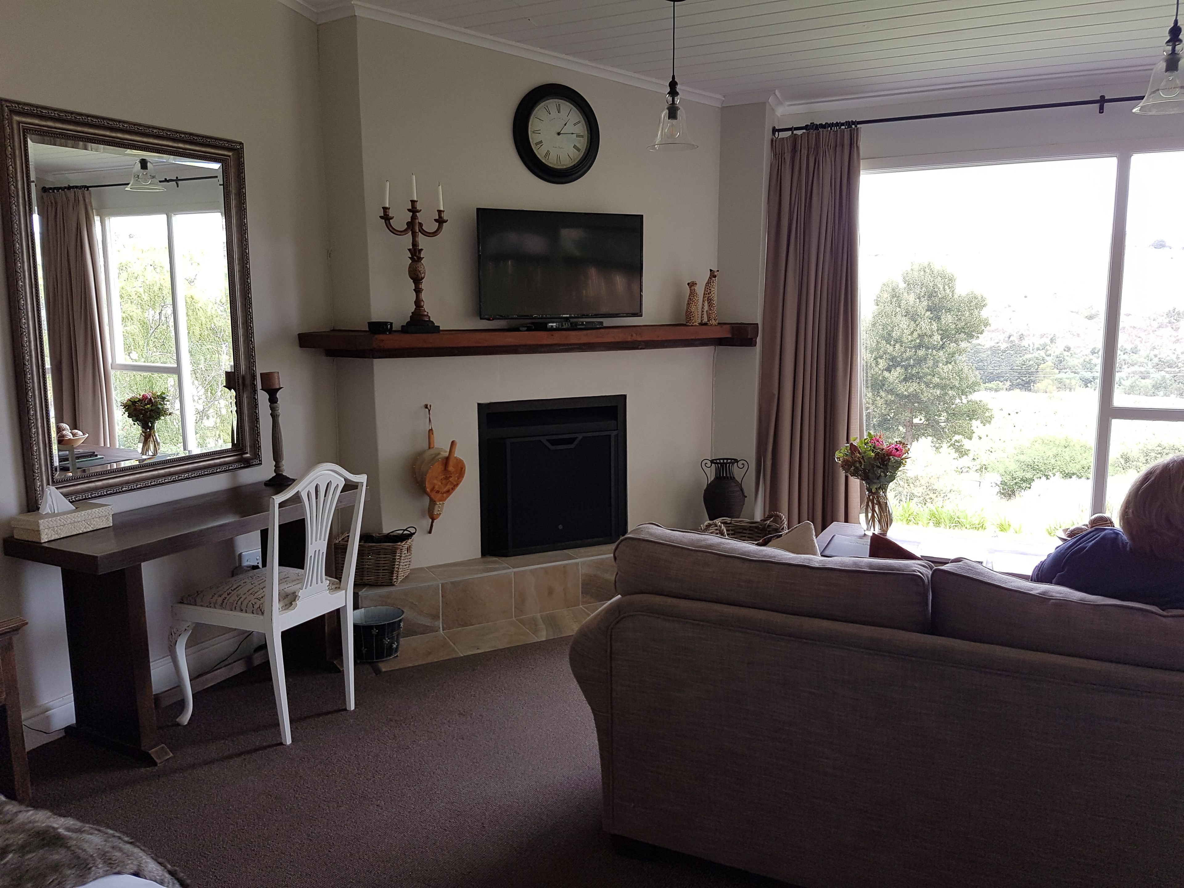 A living room with a fireplace, a television mounted above it, a large mirror, and a window with curtains.