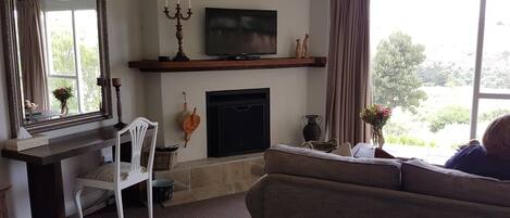 A living room with a fireplace, a television mounted above it, a large mirror, and a window with curtains.