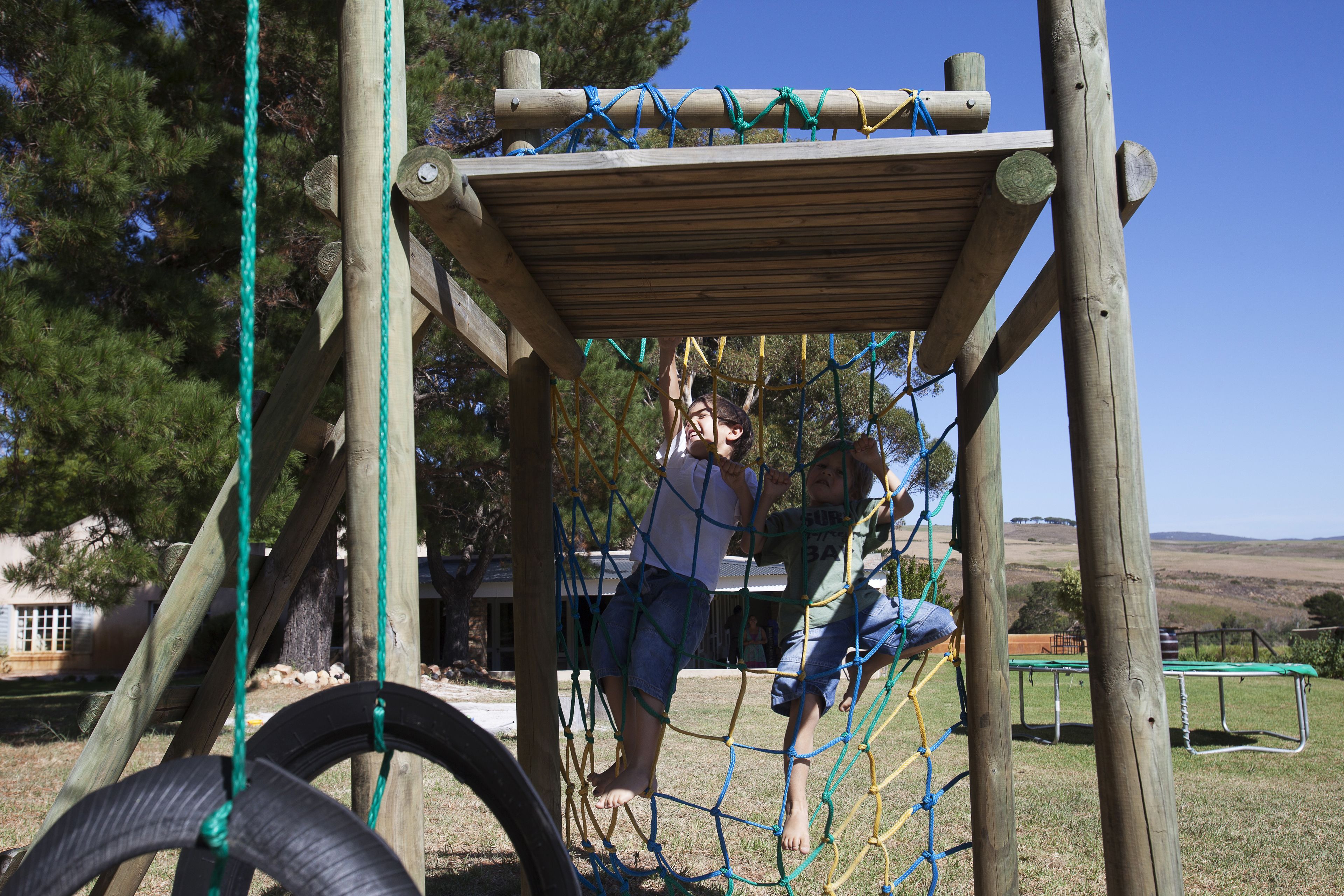 A wooden play structure with netted climbing areas and a picnic table in the background.