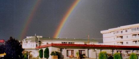 A hotel with a red roof, a parking lot, and a visible rainbow in the background.
