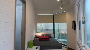 A narrow hallway with a bed at the end, a small table, and a window with a view. - B my guesthouse - Hostel (Seoul)