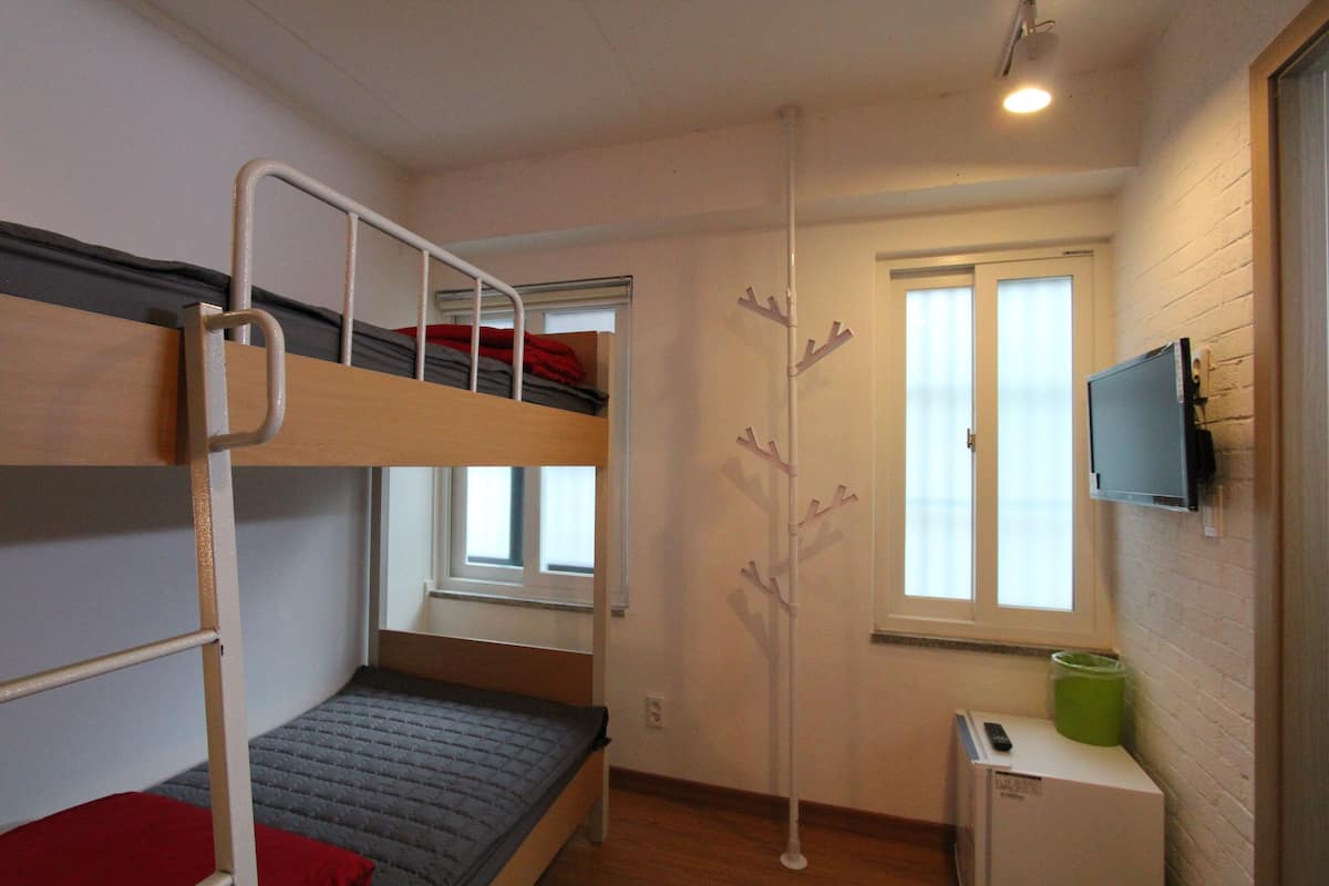 A bunk bed room with a TV, a small cabinet, and a window.