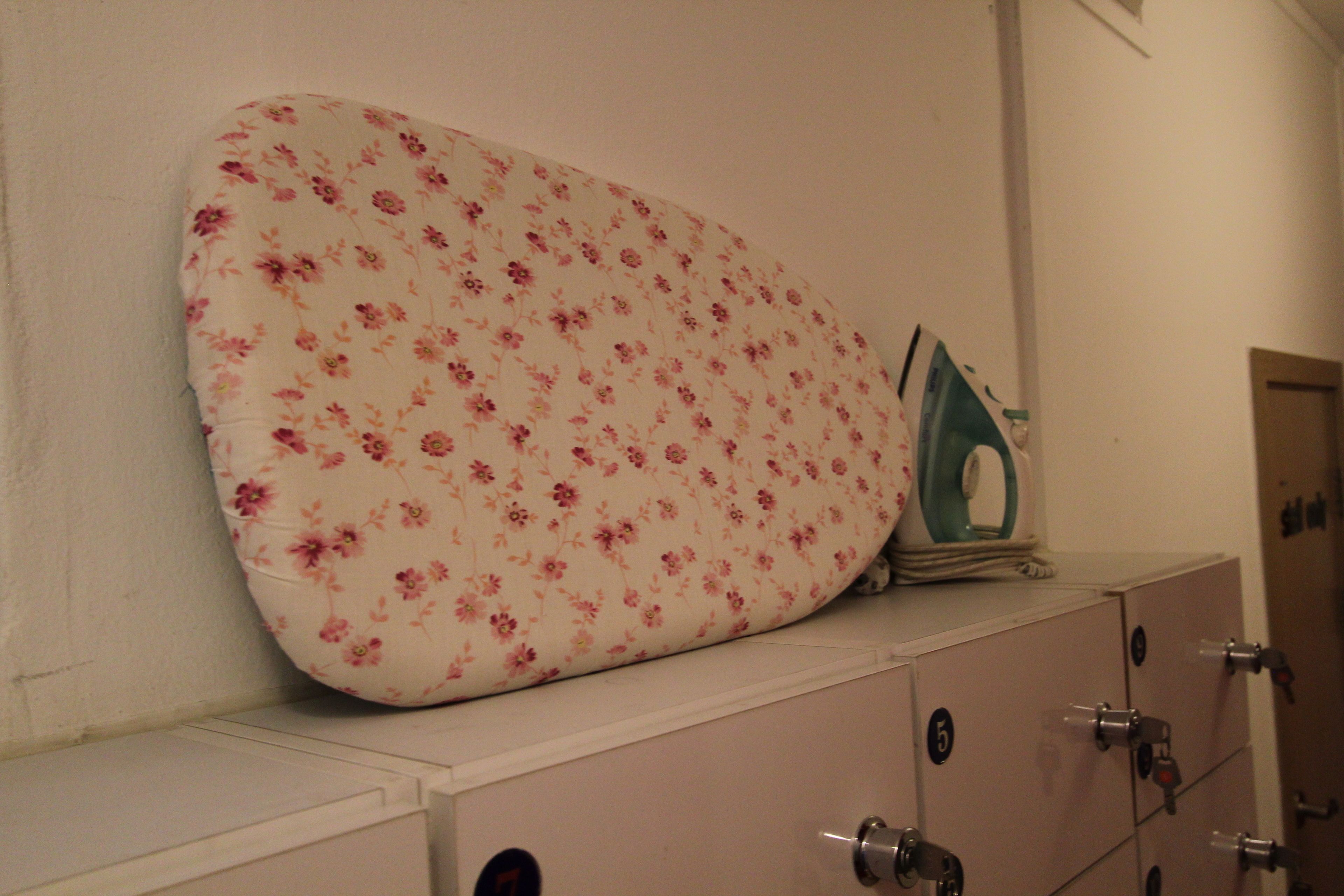 A storage unit with a floral-patterned ironing board and an iron.