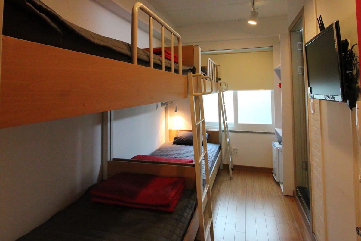 A bunk bed room with a wooden floor, a desk with a chair, and a television mounted on the wall.