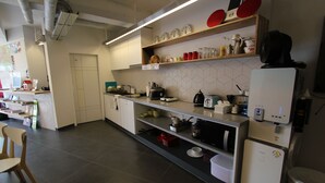 A modern kitchen with white cabinets, a built-in oven, and a coffee machine. There are shelves with dishes and kitchen utensils. - B my guesthouse - Hostel (Seoul)