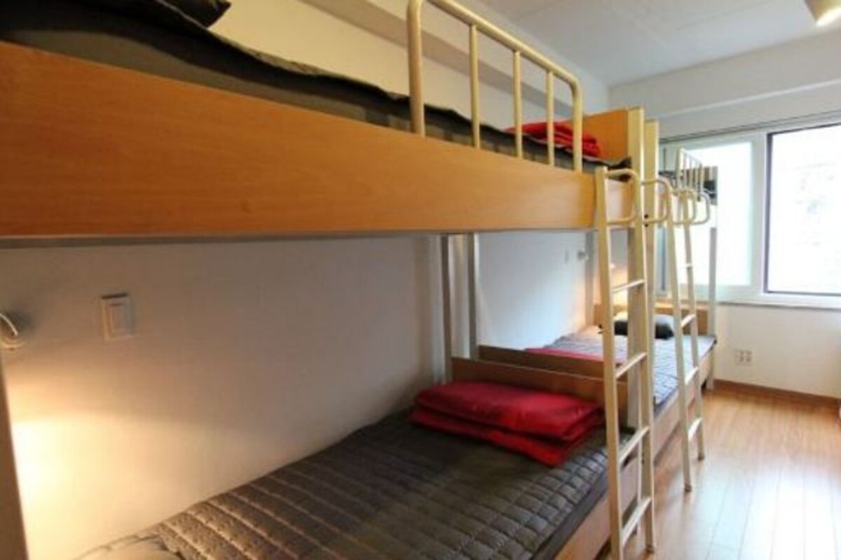 A bunk bed room with a window and a wooden floor.