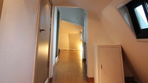 A hallway with wooden flooring, a door on the left, and a small window on the right. - B my guesthouse - Hostel (Seoul)