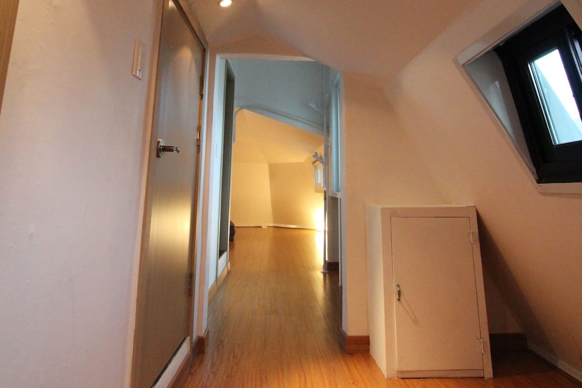 A hallway with wooden flooring, a door on the left, and a small window on the right.