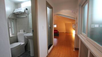 A narrow hallway with a bathroom on the left, a wooden floor, and a staircase leading to a lower level.