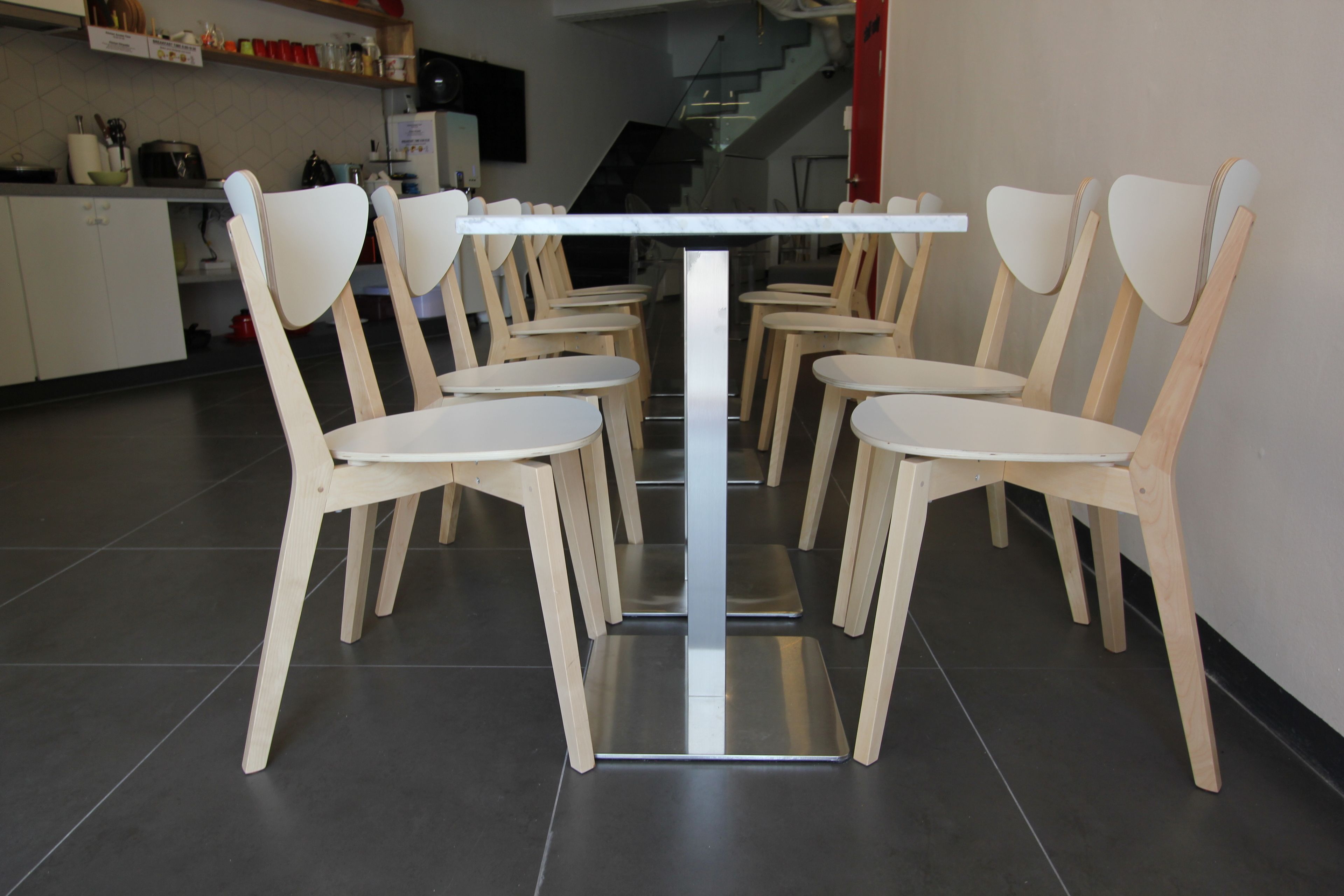 A modern kitchen with white cabinets, a stainless steel refrigerator, and a wooden dining table with six chairs.