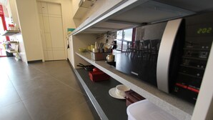 A kitchen with a microwave, a coffee maker, and a sink. There are chairs and a table in the background. - B my guesthouse - Hostel (Seoul)